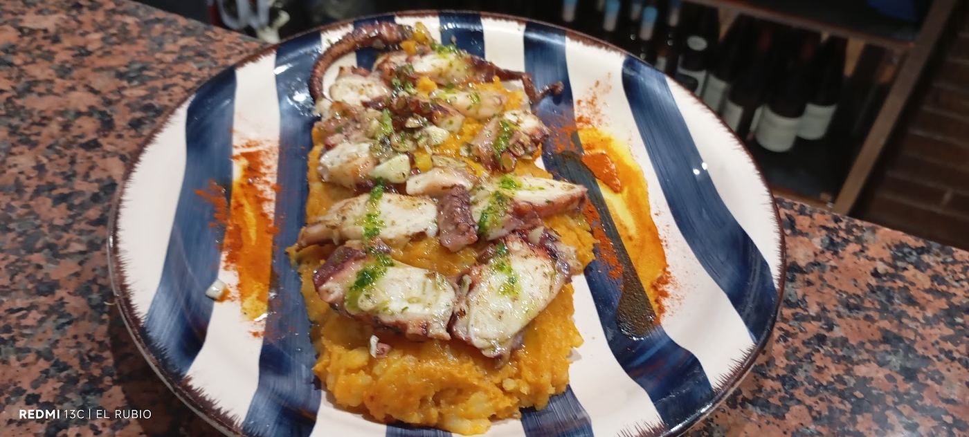 Pulpo a la gallega con puré de patatas, presentado en tabla de madera.